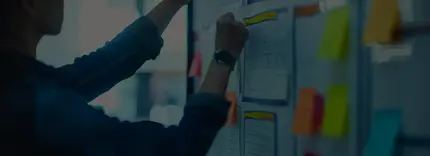 A presenter pointing to post-it notes and other papers on a board.